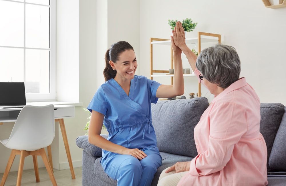 Cheerful caregiver sharing a high five with a smiling senior client